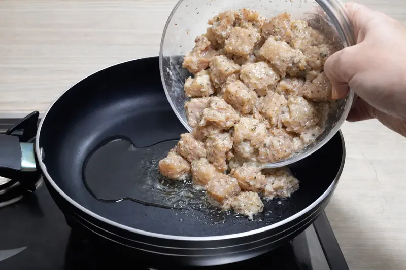 Marinated chicken being added to heated oil in frying pan