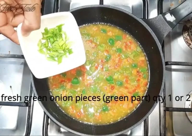 Chopped spring onions added to orange vegetable sauce