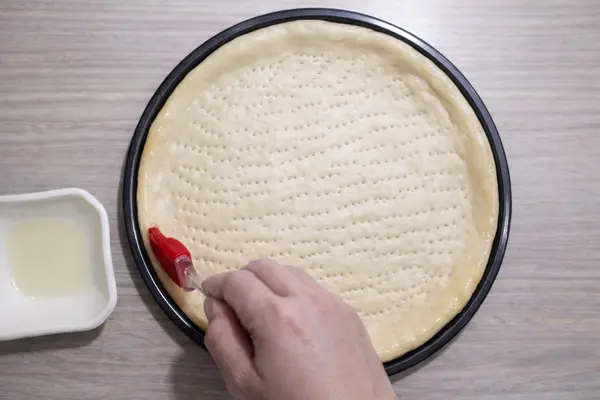 Applying oil to pizza crust edges to keep them soft during baking