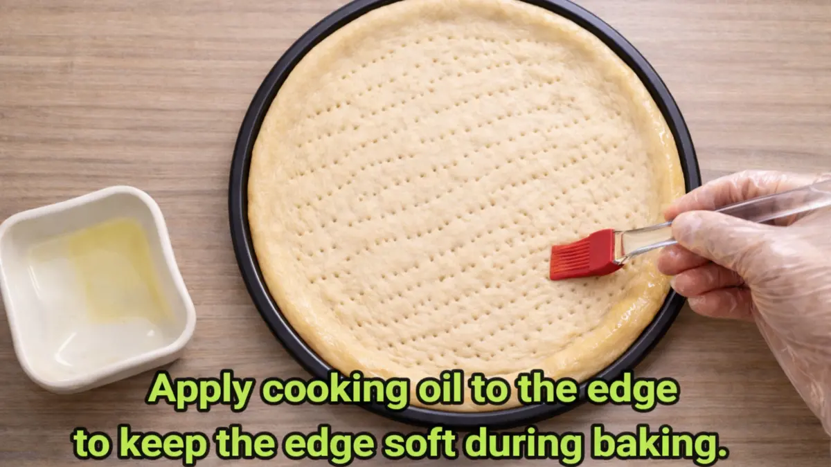 Applying cooking oil to the edge of pizza crust with a brush to keep it soft during baking