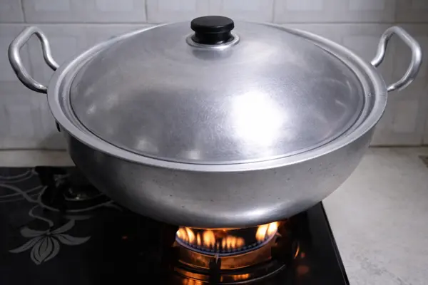 Pizza baking inside covered wok on high flame on a stovetop