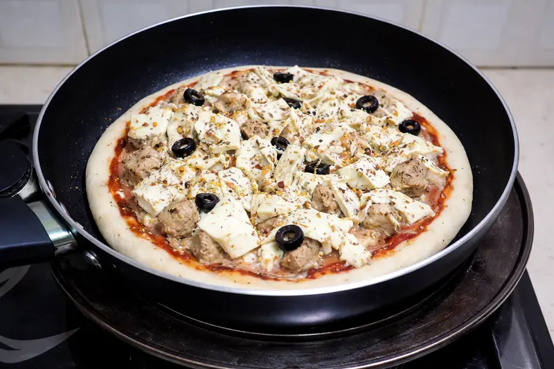 Unbaked pizza placed inside heavy-bottom pan for stovetop baking