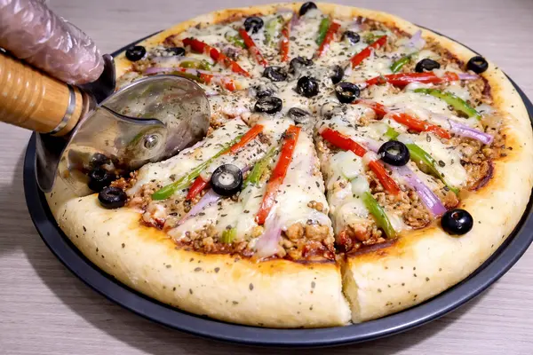 Cutting freshly baked chicken mince pizza with pizza cutter
