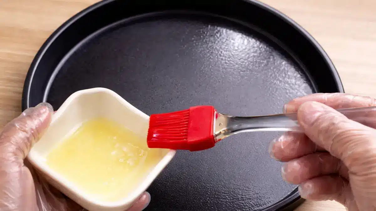 Applying cooking oil to a pizza pan using a silicone brush to prevent sticking
