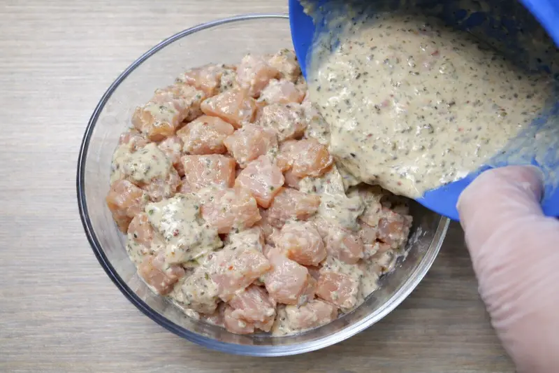 Chicken cubes coated with yogurt, garlic, and spice marinade in mixing bowl