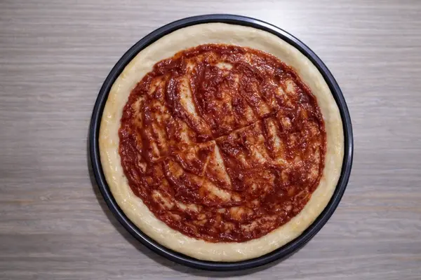 Pizza sauce spread evenly on pizza base leaving edges clear