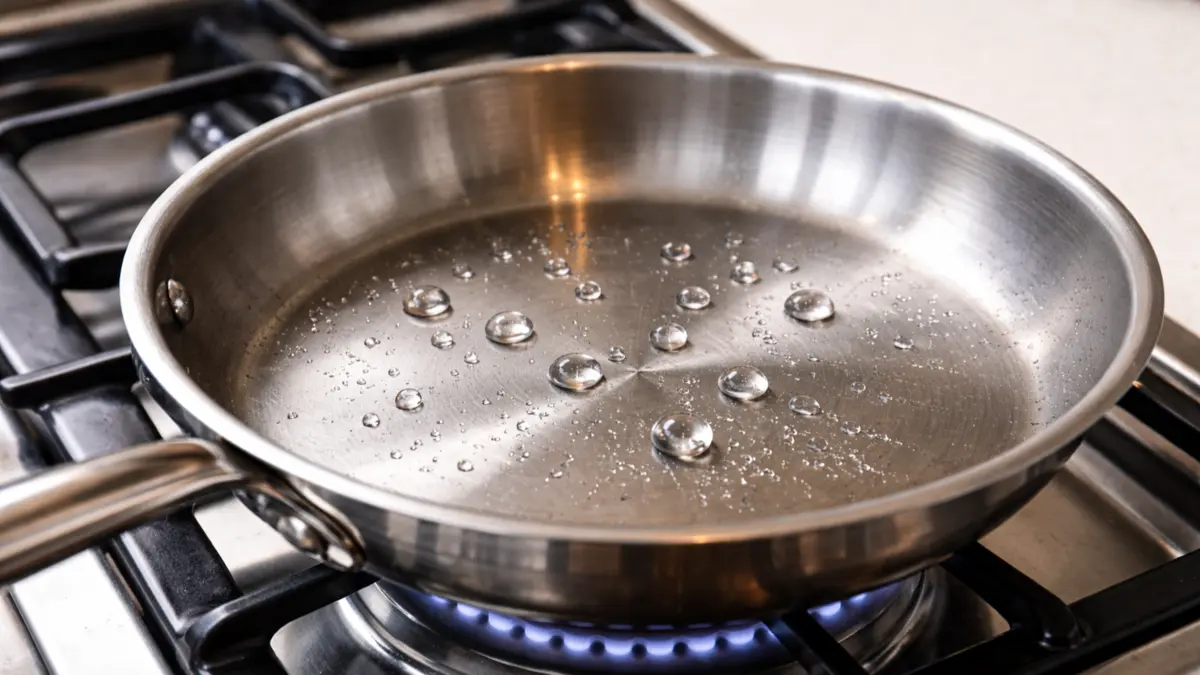 Water droplets sizzling and dancing on a hot stainless steel pan surface