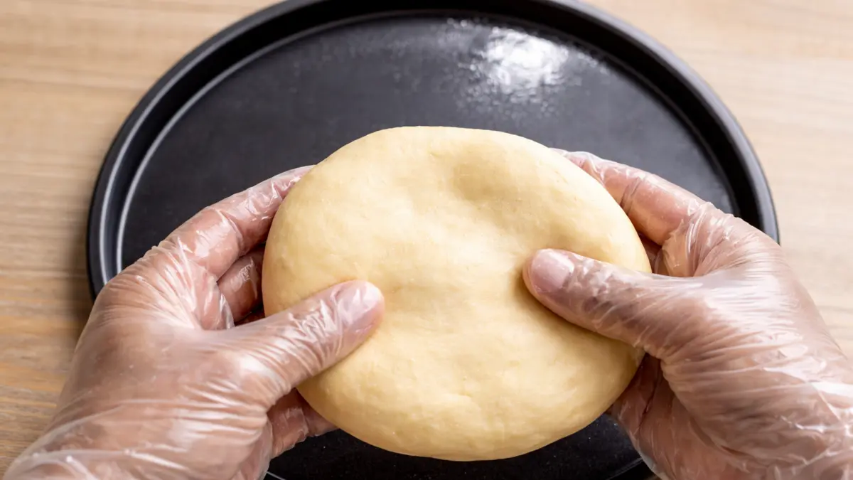 Stretching a soft pizza dough ball evenly by hand before placing it in the baking pan